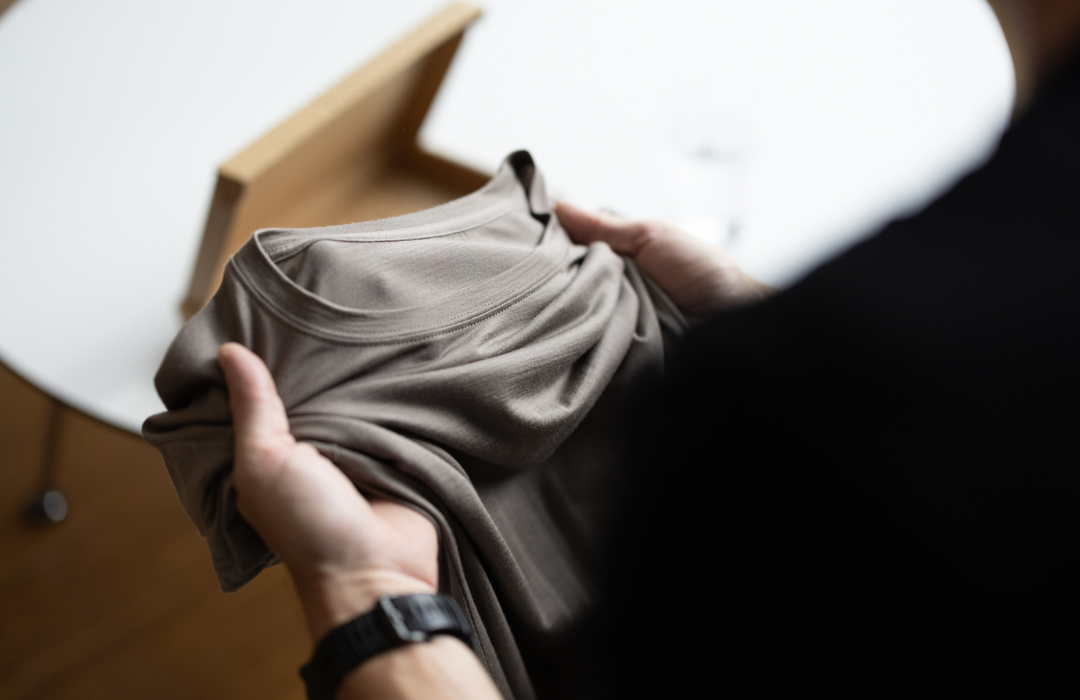 Hænder holder en sandfarvet merino-T-shirt fra LOOW